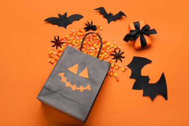 Kağıt torbalı kompozisyon, hediye kutusu ve turuncu arka planda Cadılar Bayramı için lezzetli mısır şekeri.