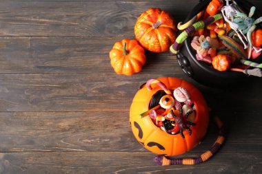 Dekoratif balkabağı ve siyah ahşap zemin üzerinde farklı tatlı şekerlemeler bulunan kazan. Cadılar Bayramı