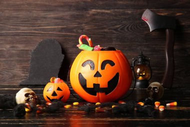 Farklı tatlı şekerlerle süslü balkabakları ve siyah ahşap masa üzerinde kafatasları. Cadılar Bayramı