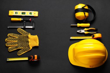 Sert şapka, koruyucu kulaklıklar ve siyah arka planda inşaat aletleri, üst görünüm