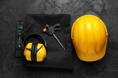 Sert şapka, koruyucu kulaklıklar, üniforma ve inşaat aletleri siyah grunge arka plan, üst görünüm