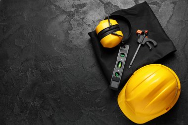 Sert şapka, koruyucu kulaklıklar, üniforma ve inşaat aletleri siyah grunge arka plan, üst görünüm