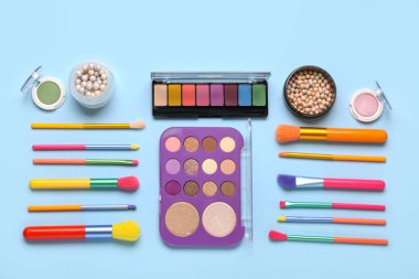 Mavi zemin üzerinde farklı makyaj fırçaları ve kozmetik ürünleri olan kompozisyon