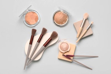 Beyaz arka planda farklı makyaj fırçaları, sıva podyumları ve kozmetik ürünleri olan kompozisyon