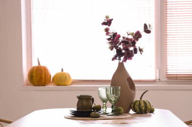 Okaliptüs dallı vazo, kabak ve tabaklar yemek masasında.