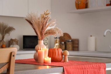 Çimenli vazo, sonbahar dekoru ve mutfak masasında yanan mumlar.
