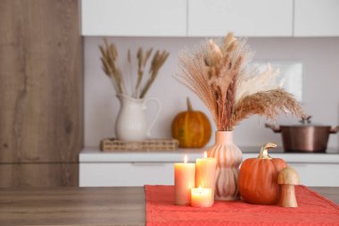 Çimenli vazo, sonbahar dekoru ve mutfak masasında yanan mumlar.