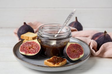 Kavanozlu tatlı incir reçeli ve beyaz ahşap masada lezzetli tostlar, yakın plan.