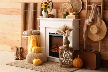 Katlanır ekran, merdiven, bavul, hasır masa ve ahşap duvarın yanındaki şöminede sonbahar süslemeleri olan oturma odasının içinde.