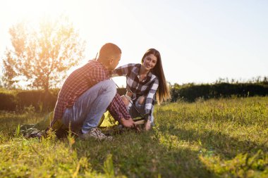 Genç çift nehir kenarında kamp için çadır kuruyor.
