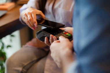 Happy young woman making payment through mobile phone in cafe