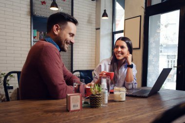 Young couple sitting in a cafe, drinking coffee and using laptop.