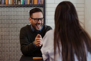 Smiling man talking to his girlfriend while she is sitting in cafe