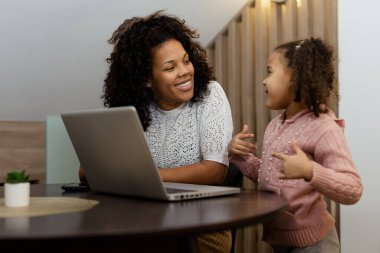 Evde dizüstü bilgisayar kullanan mutlu bir anne ve kızın portresi.