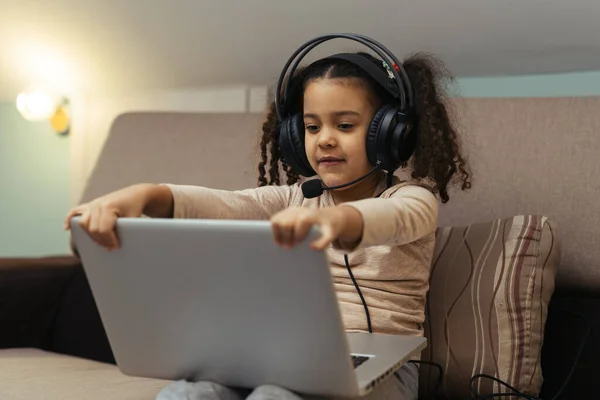Kanepede Dizüstü Bilgisayarla Oturan Kulaklıklı Mutlu Küçük Kız — Stok fotoğraf