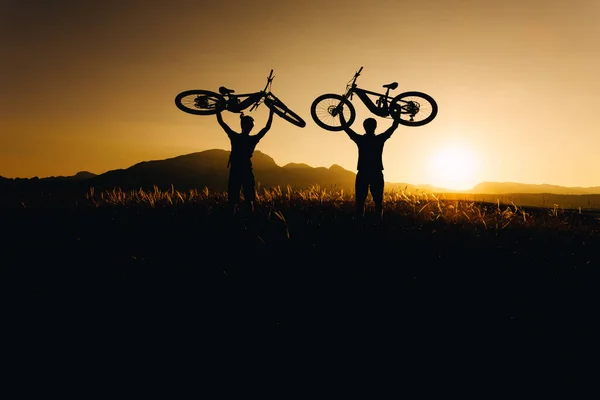 Bike adventure in the mountains. Silhouette of a bikers picking up his bike at sunset