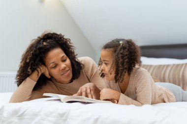 Evde yatakta uzanmış kitap okuyan anne ve kızın portresi.