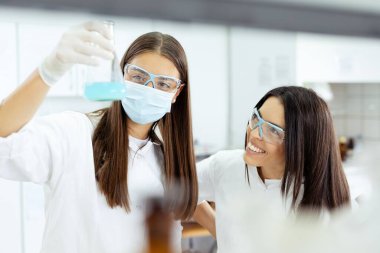 Laboratuvarda iki bilim adamı mavi bir sıvı örneğini inceliyor..