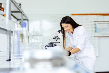 Beyaz önlüklü kadın bilim adamı mikroskop altında tam donanımlı, modern bir laboratuvarda kesin bilimsel keşif ve araştırma metodolojisini vurgulayan bir örnek üzerinde çalışıyor..