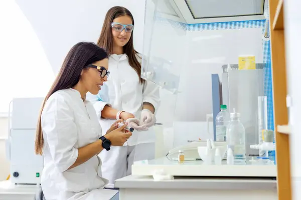 Stock image Two female scientists in a laboratory, engaged in scientific work wearing protective goggles and using equipment, demonstrating a collaborative research environment.