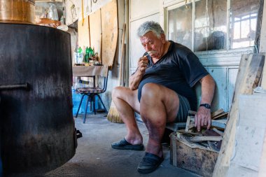 Bir adam damıtma işlemine devam edebilmek için kazanda ateş yakar.