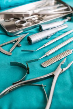 Tıbbi işlemler ve cerrahi müdahaleler için gerekli aletleri gösteren titizlikle bir deniz mavisi kumaşı üzerinde düzenlenmiş hassas cerrahi aletlerin bir koleksiyonu..