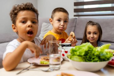 Masada üç genç çocuğun olduğu canlı bir sahne, taze yeşillikler içeren ortak bir yemeğin tadını çıkarıyor, beraberlik ve neşe duygusunu teşvik ediyor..