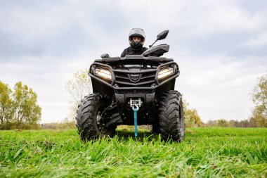Bulutlu bir gökyüzünün altında yemyeşil bir alanda gezinen kasklı bir sürücünün düşük açılı çekimi macera ve keşfin özünü yakalıyor..
