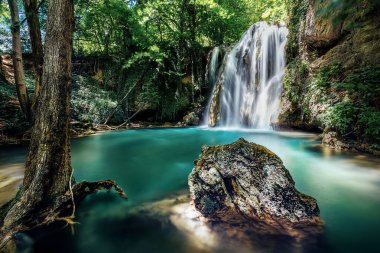 Şelalenin şelaleye uzun süre maruz kalması göz kamaştırıcı, canlı turkuaz bir gölete dönüşüyor, yemyeşil ormanlarla çevrili.