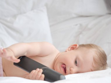 Küçük şirin bebek beyaz bir yatakta uzanıyor cep telefonuyla