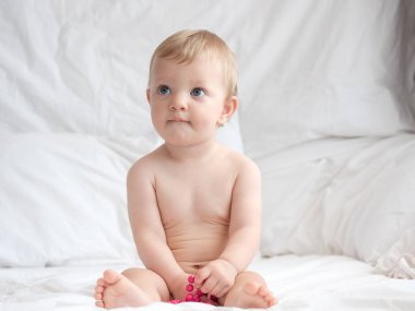 Bebek yatakta oturuyor ve boncuklarla oynuyor.