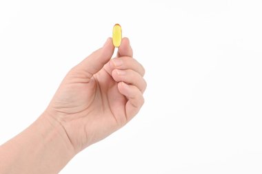 A hand holding a small yellow pill. The pill is labeled with the word 