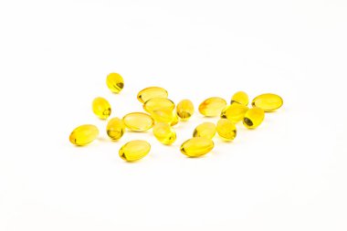 A bunch of yellow pills are scattered on a white background. The pills are small and oval-shaped, and they are all the same color. Concept of organization and uniformity