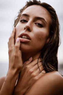 Yaz tatili konsepti. Güzel, genç, seksi bir kadın. Eğitimli, zayıf vücutlu ve ıslak saçlı. Sahilde yakın plan bir portre. Moda kadın modeli deniz kenarında poz veriyor.