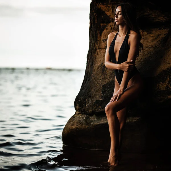 夏季娱乐的概念 身穿黑色泳衣比基尼 身材匀称 训练有素 身材纤细的年轻貌美女子站在海滩上的水里 时尚女模特在海里摆姿势 — 图库照片