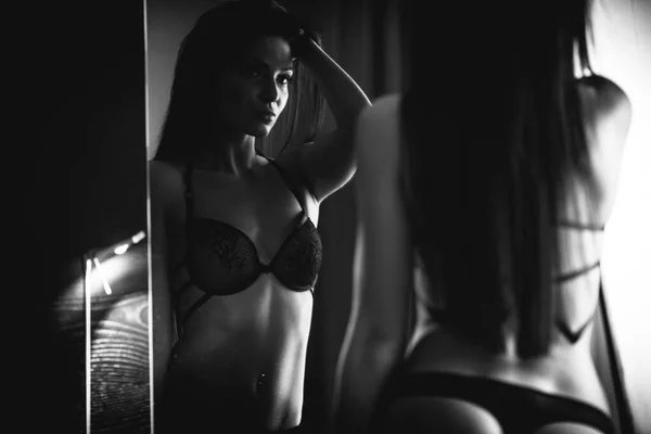 女性の体とランジェリーのコンセプトの美しさ 高級ホテルの部屋ではセクシーな黒の下着姿で美しい女性モデルがポーズ 少女はブラとパンティーを着た鏡の前に立つ 白黒モノクロームで — ストック写真