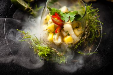 Mango, acı biber ve kişniş soslu scallop ceviche bir tabakta sıvı buz dumanı ile servis edilir. Modern gurme mutfağındaki bir masada öğle yemeği olarak sunulan lezzetli ve sağlıklı yiyecekler..
