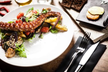 Sıcak ahtapot salatası, kızarmış sebzeler ve beyaz tabakta ji sosu. Lezzetli, sağlıklı, geleneksel deniz ürünleri modern mutfak gurme restoranında öğle yemeği için bir masada servis edilir.
