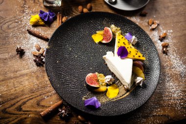 Tutkulu meyveli cheesecake, incir ve portakal tabakta. Modern gurme mutfağındaki bir masada öğle yemeği olarak sunulan lezzetli ve sağlıklı yiyecekler..