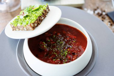 Borş çorbası. Siyah Angus bifteği, pancar kökü, ekşi krema, kase içinde çiçek olan kızarmış ekmek. Modern gurme mutfağındaki bir masada öğle yemeği olarak sunulan lezzetli ve sağlıklı yiyecekler..