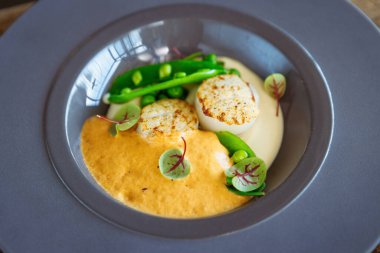 Karides köpüklü deniz tarağı, karnabahar kreması ve tabakta yeşil bezelye. Lezzetli sağlıklı deniz ürünleri, öğle yemeği için modern gurme restoranındaki bir masada servis edilir..