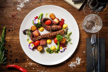 Kiraz domatesli ahtapot dokunaçları, brokoli ve yenilebilir çiçekler. Yanında kızarmış patates, sarı sos ve mikroyeşillikler var. Gurme bir restoranda sofistike deniz ürünleri yemeği..