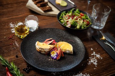İncirli ve yenilebilir çiçekli gurme peynir tabağı. Domatesli ve sebzeli taze salata. Modern bir restoranda güzel bir yemek deneyimi. Sağlıklı ve lezzetli yemek. Yakın plan..