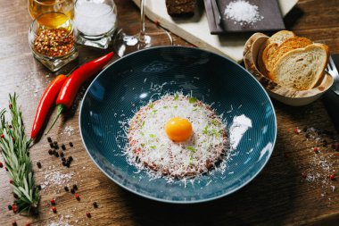 Zarif etli tart çiğ yumurta sarısı ve ince dilimlenmiş parmesanla süslenmiş. Yanında çıtır ekmek, acı biber ve taze biberiye var. Rafine mutfak sunumu için ideal..