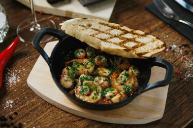 Lezzetli karides ve kabuklu ekmekle dolup taşan güzel bir tava. Kırsal bir ahşap masaya güzelce yerleştirilmiş.