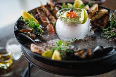 Izgara karides, midye, ahtapot ve kurutulmuş ton balığından oluşan nefis deniz ürünleri tabağı, dumanlı avokado mus, taze limon ve mikro yeşillikle servis edilir. Deniz ürünleri aşıkları için mükemmel bir gurme yemeği..