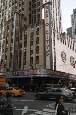 New York, ABD - 8 Nisan 2024: Radio City Music Hall 'da canlı bir sokak sahnesi. İkonik Art Deco mekanı, neon ışıkları, taksiler ve yayalar Manhattan şehir merkezinin hareketli enerjisini yakalıyorlar..