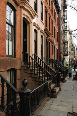 NEW YORK, ABD - 4 Nisan 2024: Greenwich Village 'da süslü demir parmaklıkları olan klasik kahverengi taştan evler. Tarihi mimari ve sakin bir kaldırım bu ikonik New York mahallesinin cazibesini yansıtıyor.