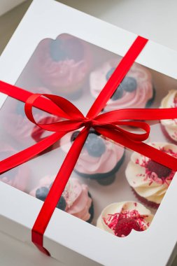 Fresh and delicious cupcakes with cheese cream and fresh berries. Top view of arranged tasty cupcakes in cardboard box isolated on white. Cakes with cream, chocolate bars, blueberries and raspberries