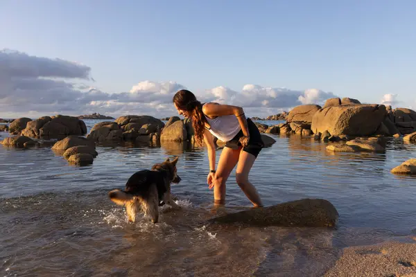 young latin woman on the beach playing with dog in the water at sunset